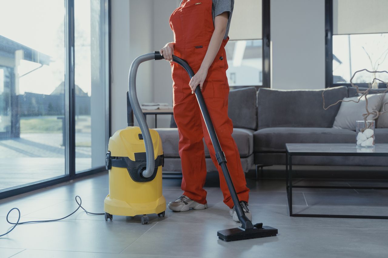 journey-01 A professional cleaner in red coveralls vacuuming a modern living room with a yellow vacuum cleaner.